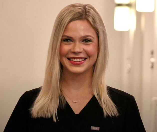 Woman smiling at camera in black top against neutral dental office background.