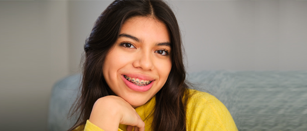 Smiling woman with long dark hair wearing yellow shirt in dental office setting