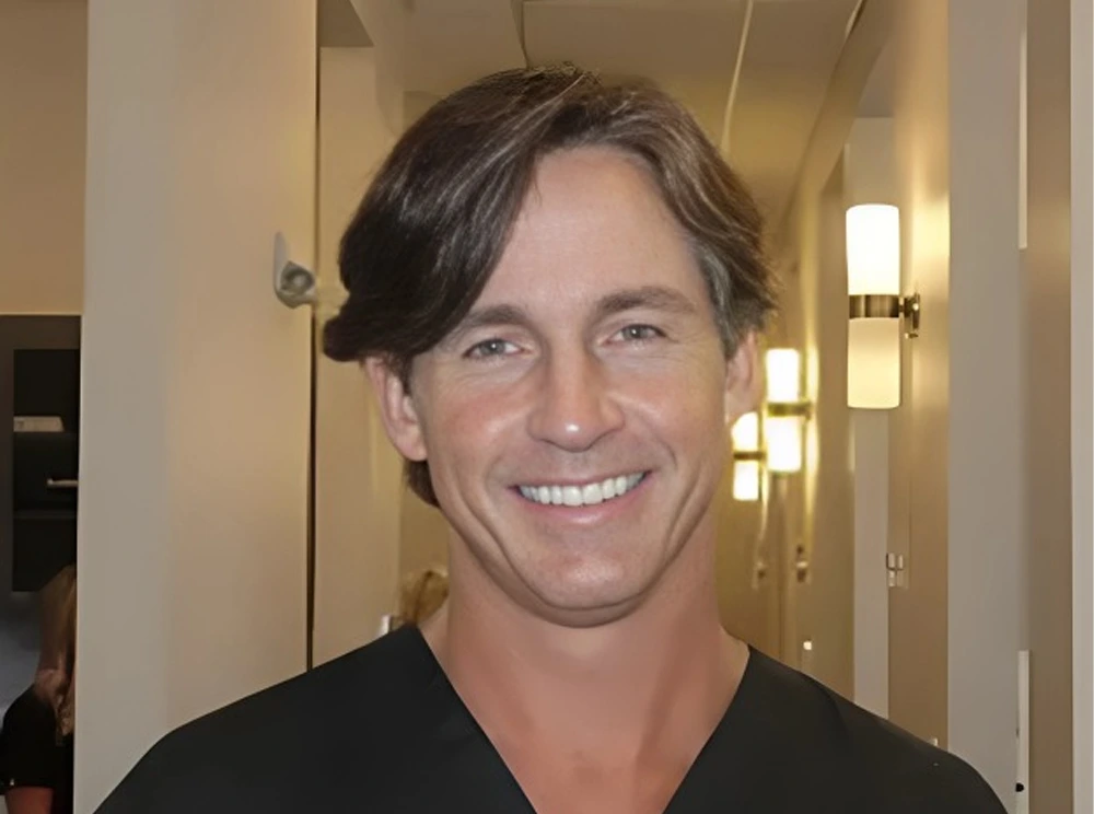 Man smiling at camera in dental office hallway wearing black shirt