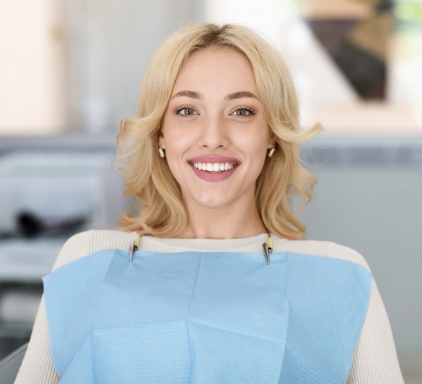 Professional woman in light blue top smiling at dental office reception area.