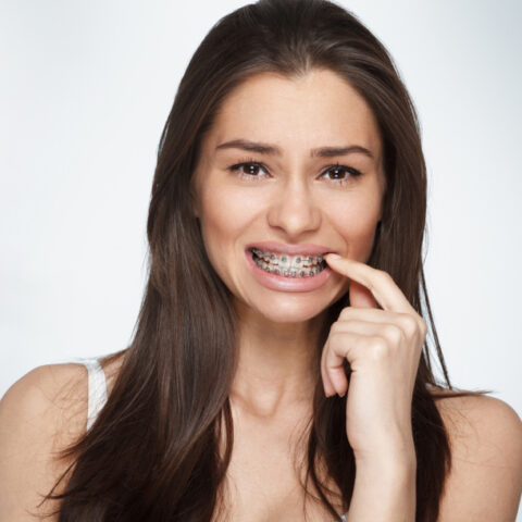 Young woman smiling while flossing teeth against white background, dental hygiene demonstration.