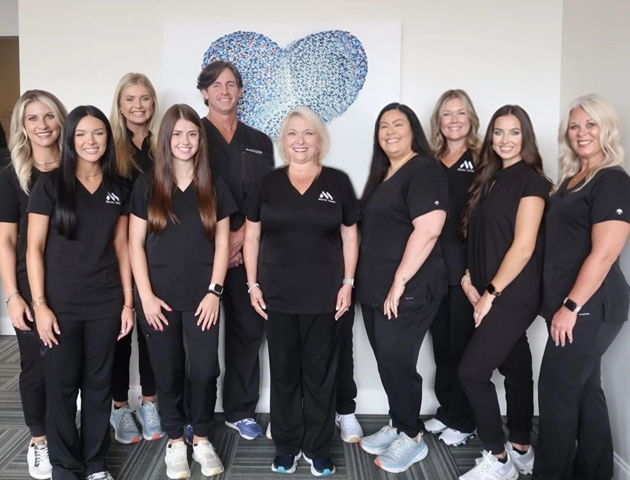 Team of dental professionals in black uniforms posing together in front of blue heart logo.